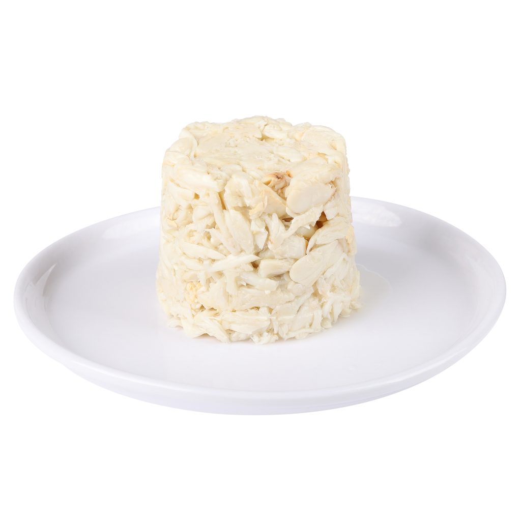 A mound of lump crab meat stacked on a white plate against a white background.