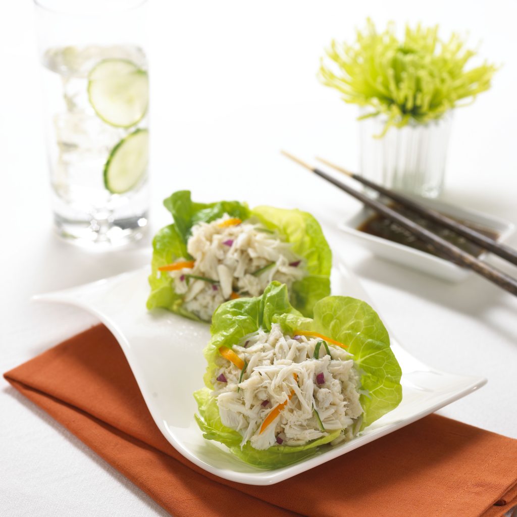 Two lettuce wraps filled with shredded crab, vegetables, and herbs on a white plate with chopsticks nearby.