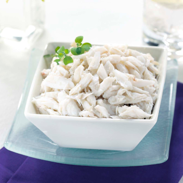 A white bowl filled with lump crab meat, garnished with a sprig of greenery, on a glass plate.